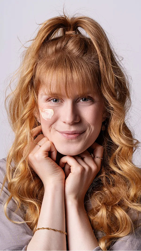 Das alva Naturkosmetik Model Paulina schaut in die Kamera und hat die Sanddorn Nachtcreme von alva Naturkosmetik auf ihrer rechten Wange aufgetragen. Sie ist glücklich.