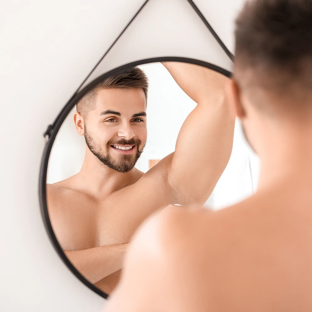 alva Naturkosmetik Model trägt alva Kristall-Deo Roll-on For Him auf Achsel auf und schaut in Spiegel, Over Shoulder Kamera Perspektive.