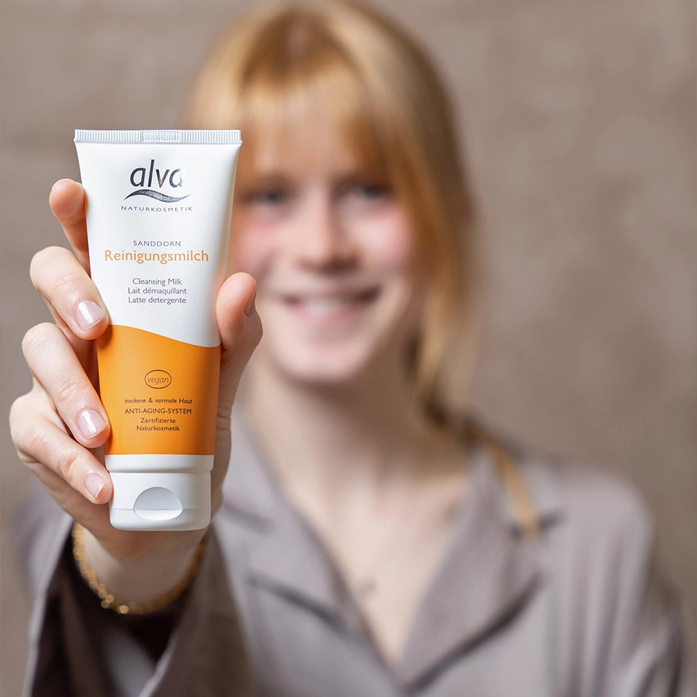 alva Sandorn Reinigungsmilch im Fokus. Im Hintergrund weibliches Model verschwommen, sie lacht in die Kamera.