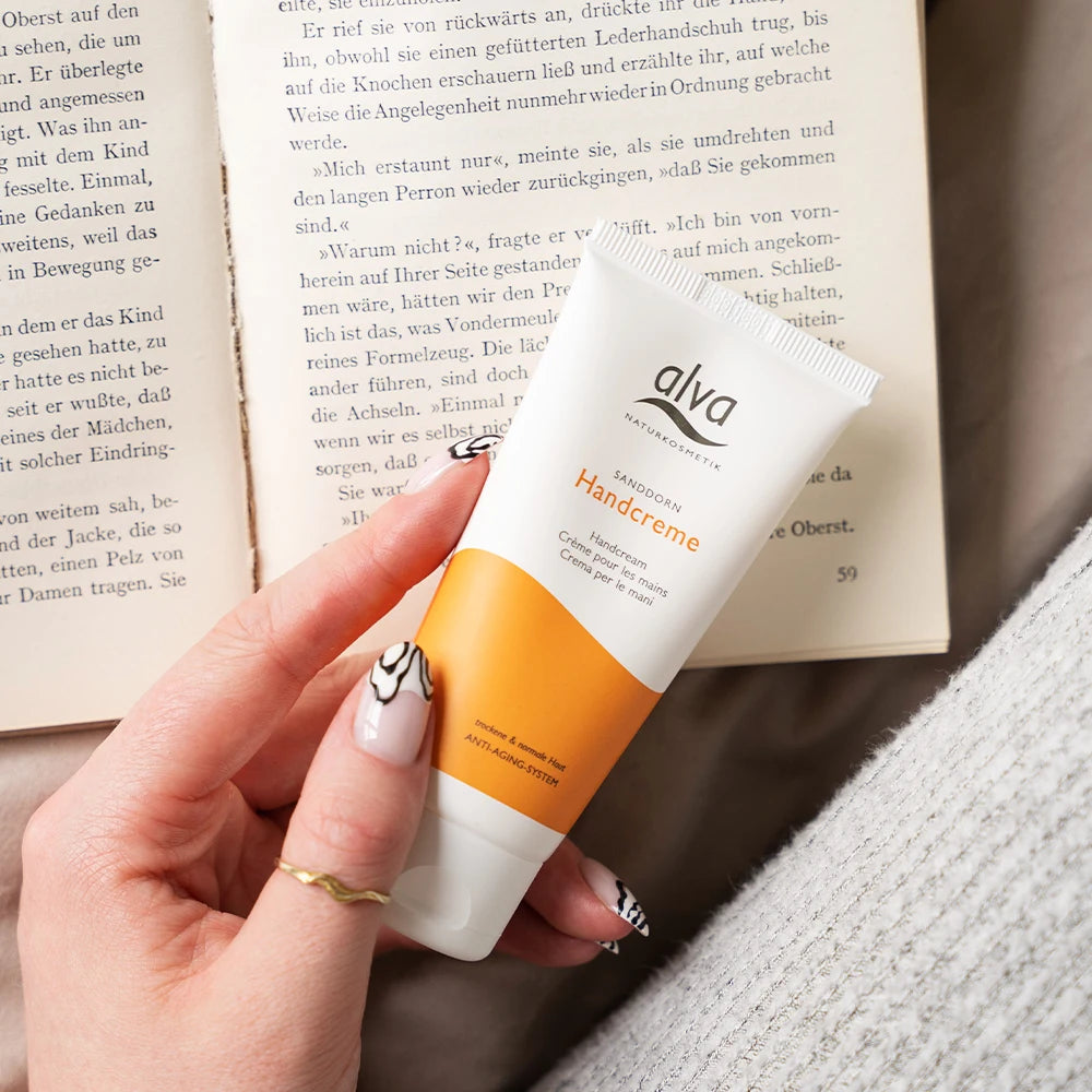 Model hält alva Handcreme Sanddorn fest. Im Hintergrund ist ein Buch zu sehen.