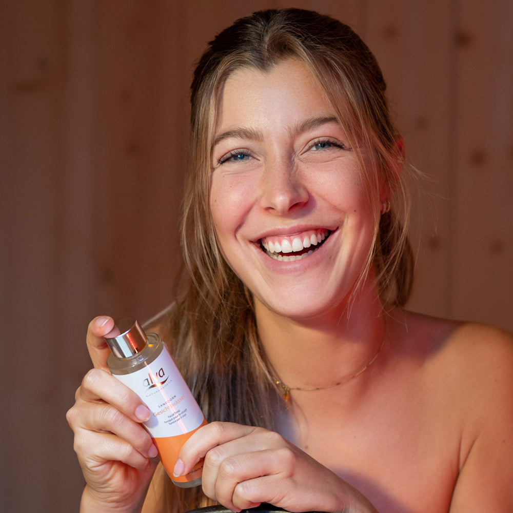 junge lachende Frau hält das alva Sanddorn Hautöl in den Händen