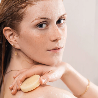 alva Naturkomsetik  Model unter der Dusche schaut in Kamera und hat alva festes Shampoo Blutorange in Hand