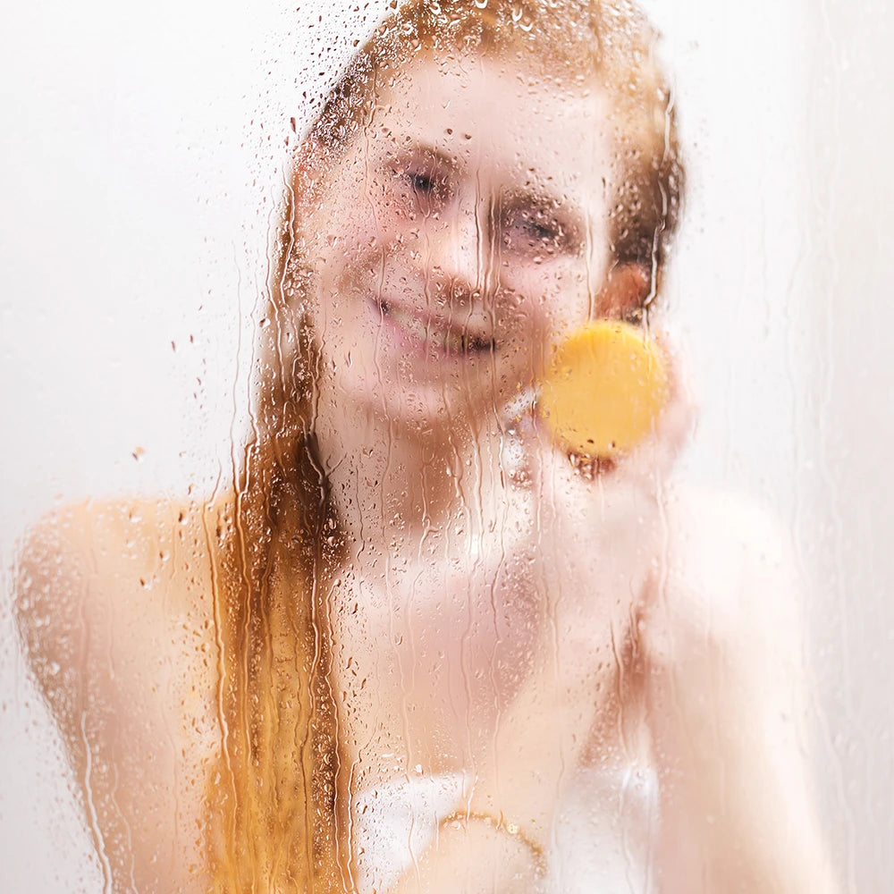alva Naturkomsetik Model unter der Dusche Nass und ist verschwommen. Sie schaut in Kamera und hat alva festes Shampoo Blutorange in Hand