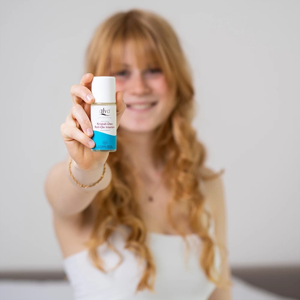 alva Naturkomsetik Model ist im Hintergrund etwas verschwommen und hält alva Kristall-Deo Roll-on intensiv Verpackung in der Hand 