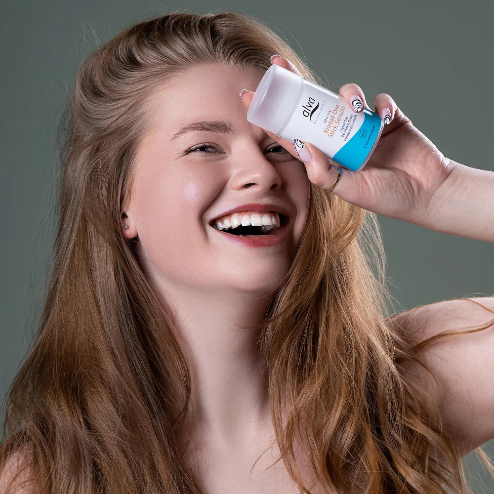 alva Model hat alva Kristall-Deo Stick sensitiv in Hand und lacht in die Kamera, close up.