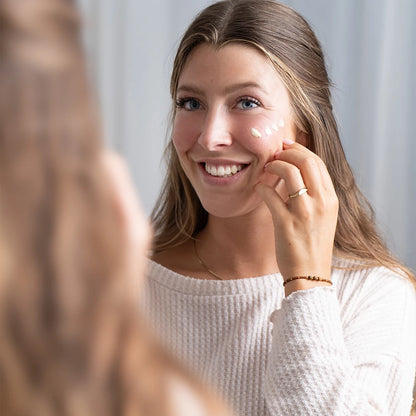 alva Naturkosmetik Model hat alva Sanddorn Feuchtigkeitscreme auf Wange aufgetragen und lacht sich im Spiegel an.