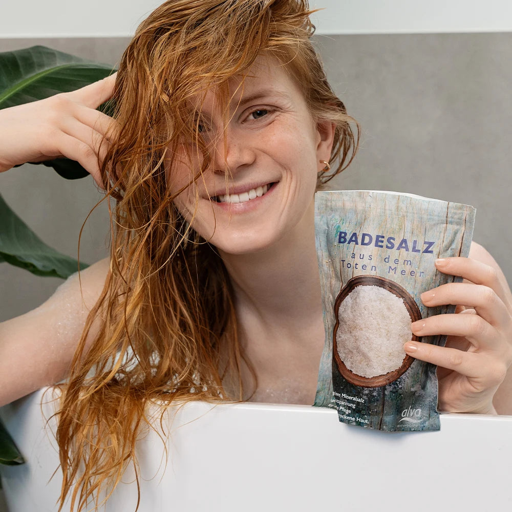Model ist in Badewanne und schaut in die Kamera. Sie hat alva Badesalz naturbelassen in der Hand. Sie ist glücklick