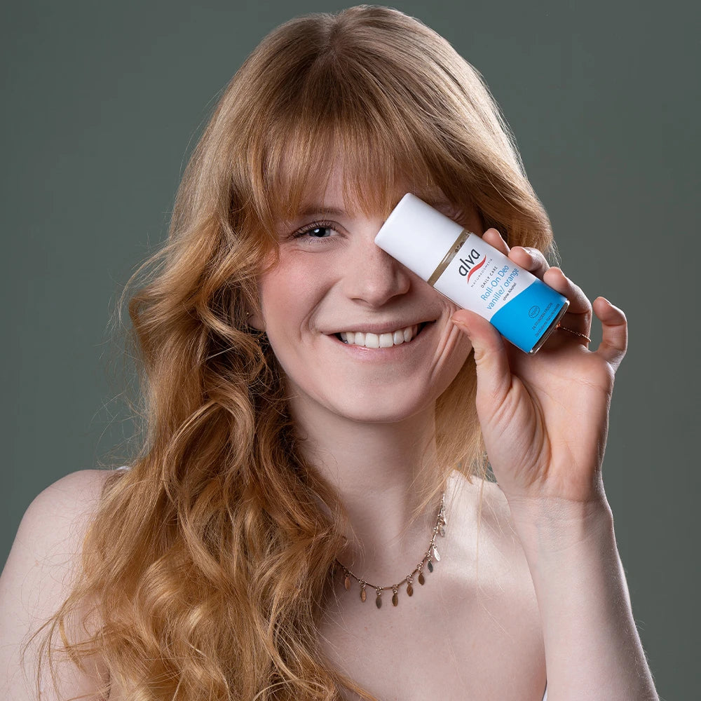 alva Naturkosmetik Model hält alva Daily Care Roll on Deo Verpackung in der Sorte vanille/orange in der Hand