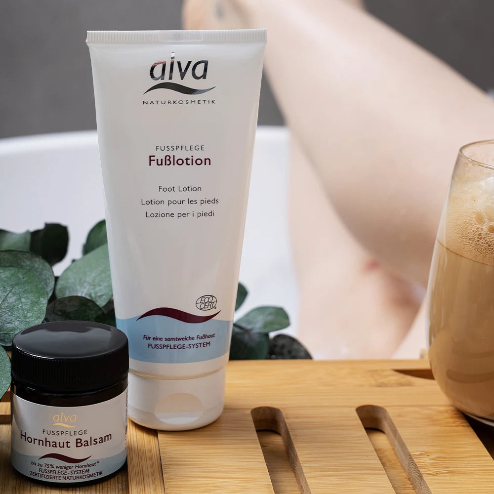 alva Hornhautbalsam und alva Fußlotion liegen auf Abstelltisch in Badewanne. Ausschnitt von Füßen im Hintergrund. Close Up
