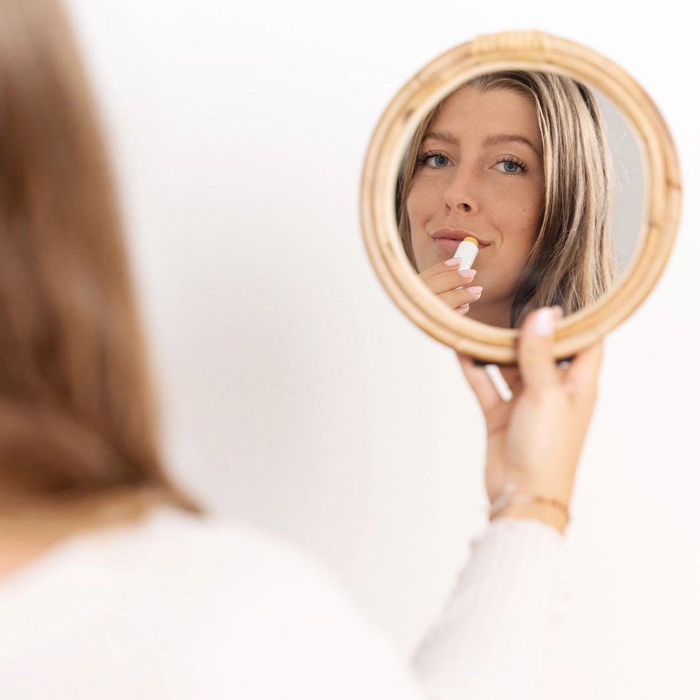 Model schaut durch den Spiegel in die Kamera und trägt sich alva Lippenbalsam Sanddorn auf Lippen auf