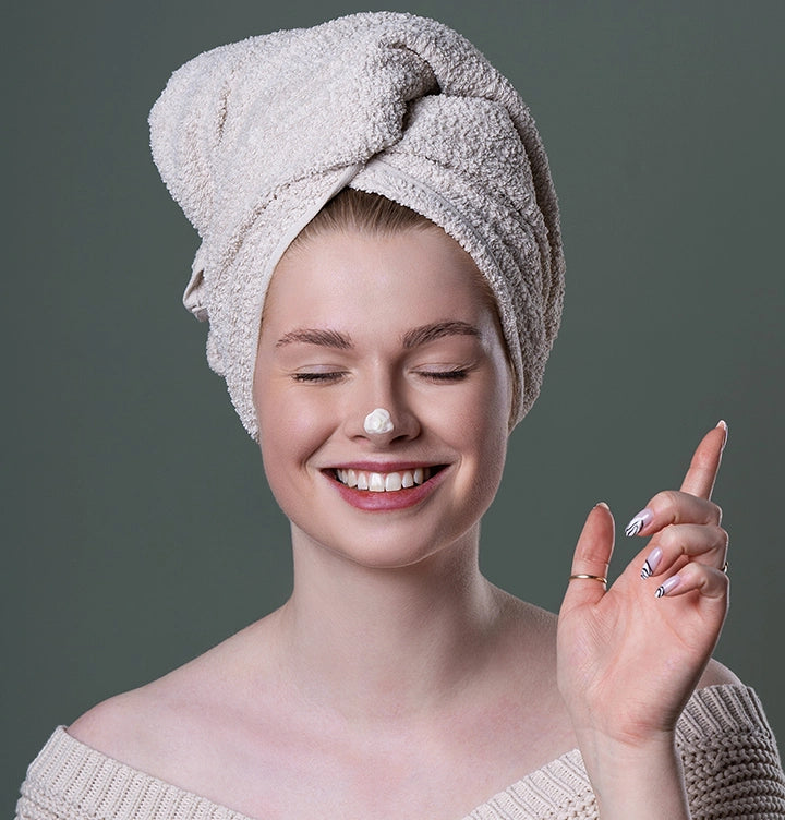 Das alva Naturkosmetik Model Emely hat einen Klecks alva Sanddorn Feuchtigkeitscreme auf ihrer Nase, sie lächelt und hat einen Turban aus einem weißen Handtuch um den Kopf gewickelt. Der Hintergrund ist dunkel Grün.