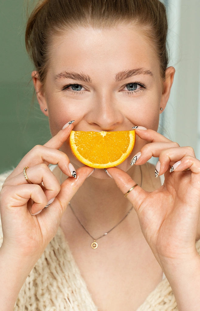 Emely das alva Naturkosmetik Model hält eine geschnittene Orange vor ihr Gesicht, dadurch sieht es so aus als ob sie lächelt. 