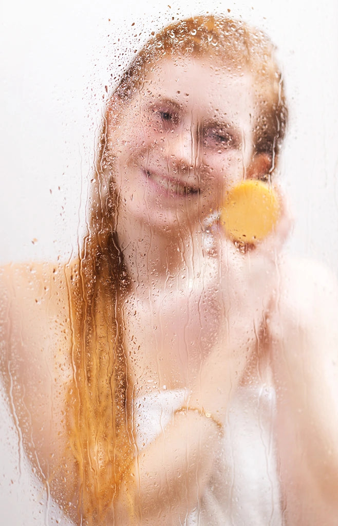 Model steht in Dusche vor nassem Glas, sie lächelt in die Kamera und hat das alva feste Shampoo in der Sorte Blutorange in der Hand.